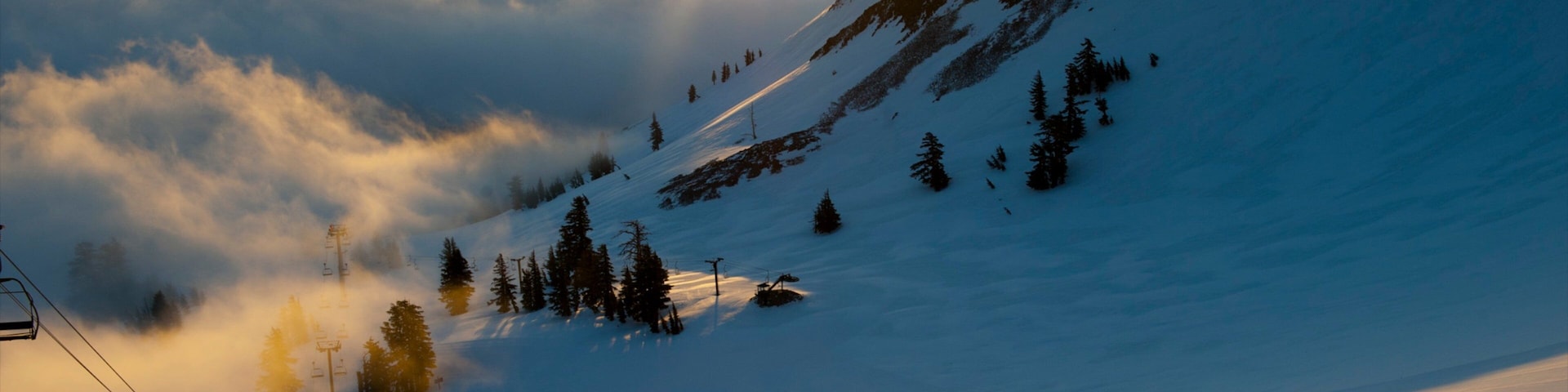 A snow-covered mountain with a ski lift and trees.