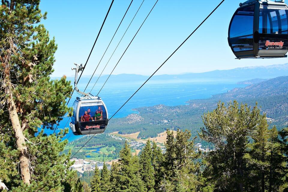 Teleférico com passageiros, paisagem montanhosa e um corpo de água ao longe.