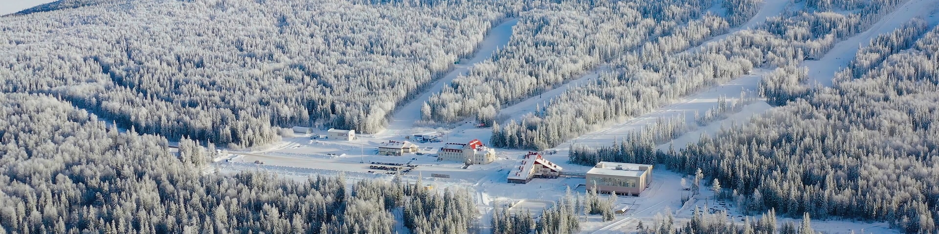 Top view of ski resort at foot of mountain. Footage. Secluded ski resort at foot of hill with ski slopes is popular in winter season. Clear sunny day on ski slopes of winter resort