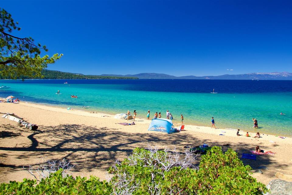 A beach with clear turquoise water, people sunbathing, and boats in the distance.