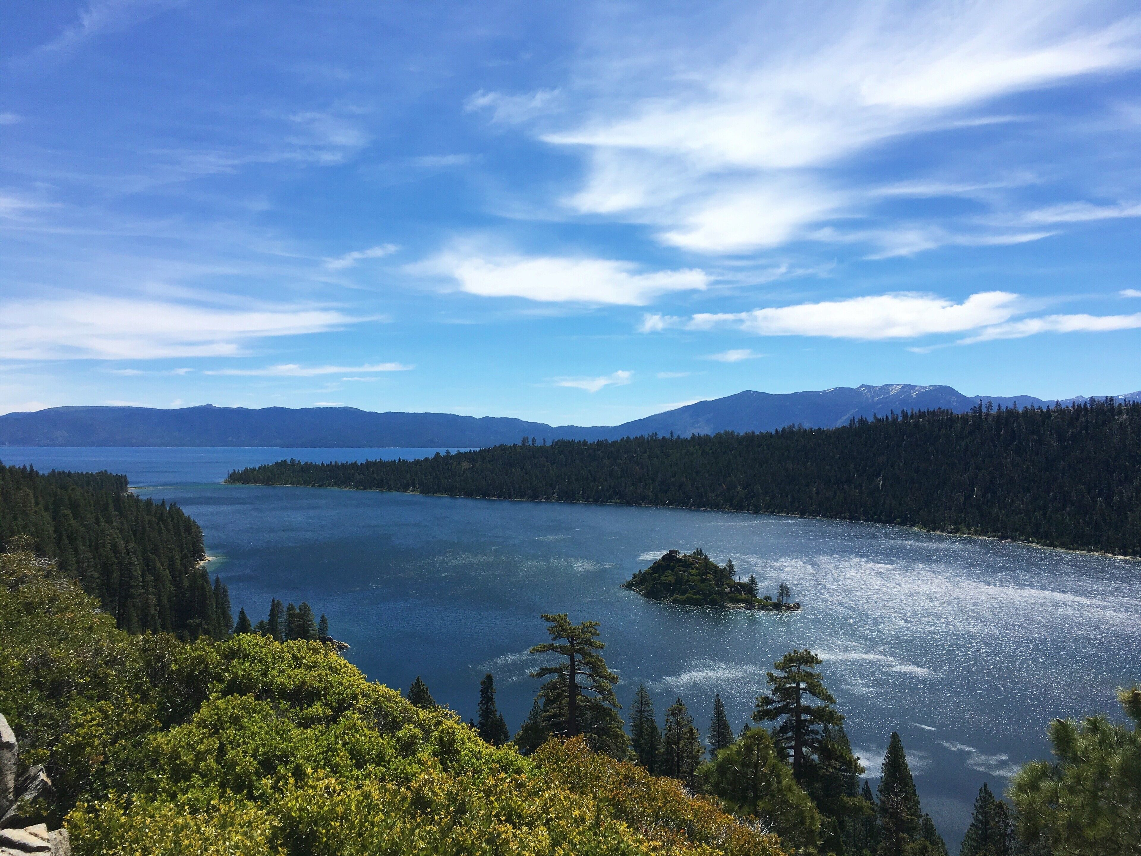 A lake surrounded by dense forests and mountains under a clear sky.