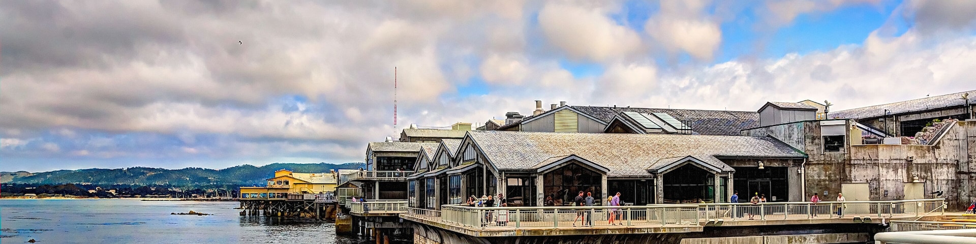 A coastal area with buildings on stilts over water, a rocky shoreline, and a cloudy sky.