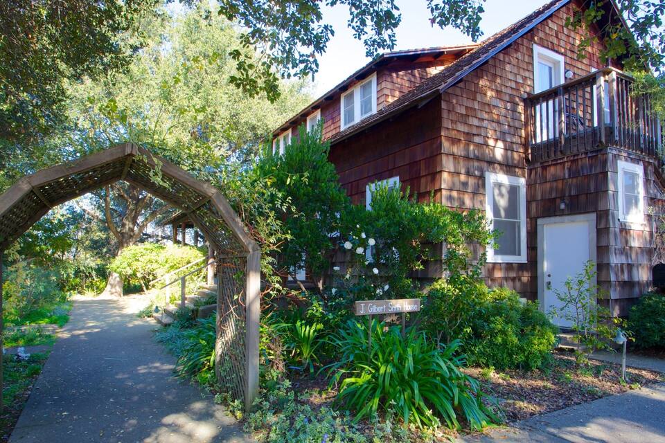 A wooden house with a porch, surrounded by lush greenery and a wooden archway.