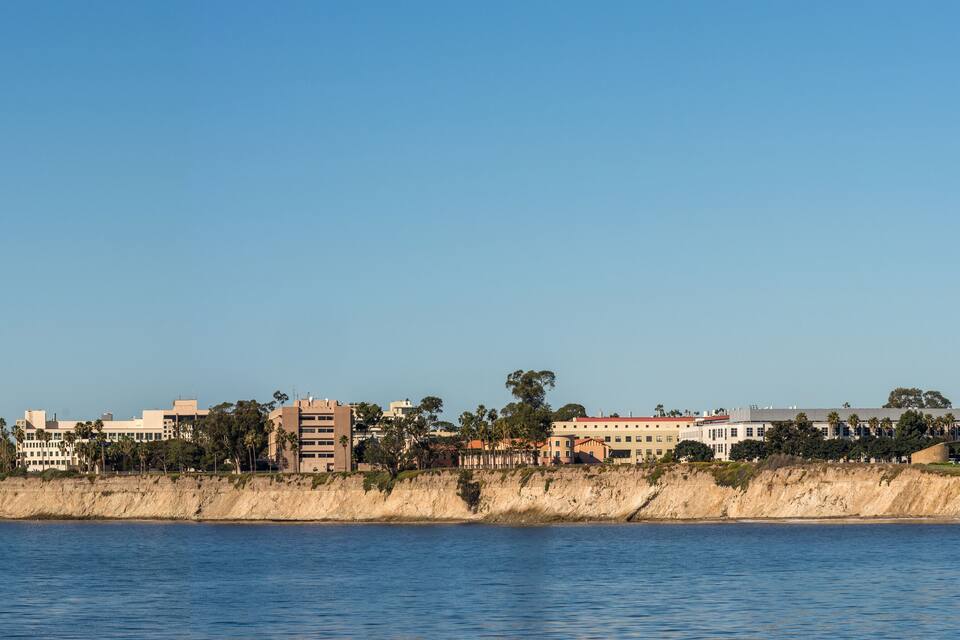 A coastal cityscape with buildings, a beach, and a clear blue sky.