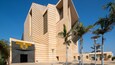 A modern building with a unique angular design, palm trees, and a clear blue sky.