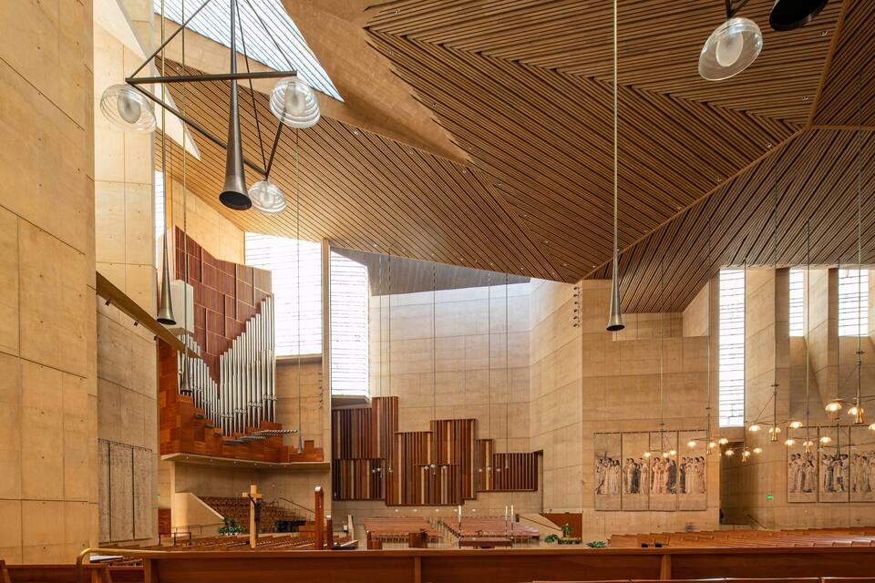 Interior de igreja moderna com bancos de madeira, um órgão grande e teto de madeira com luminárias pendentes.