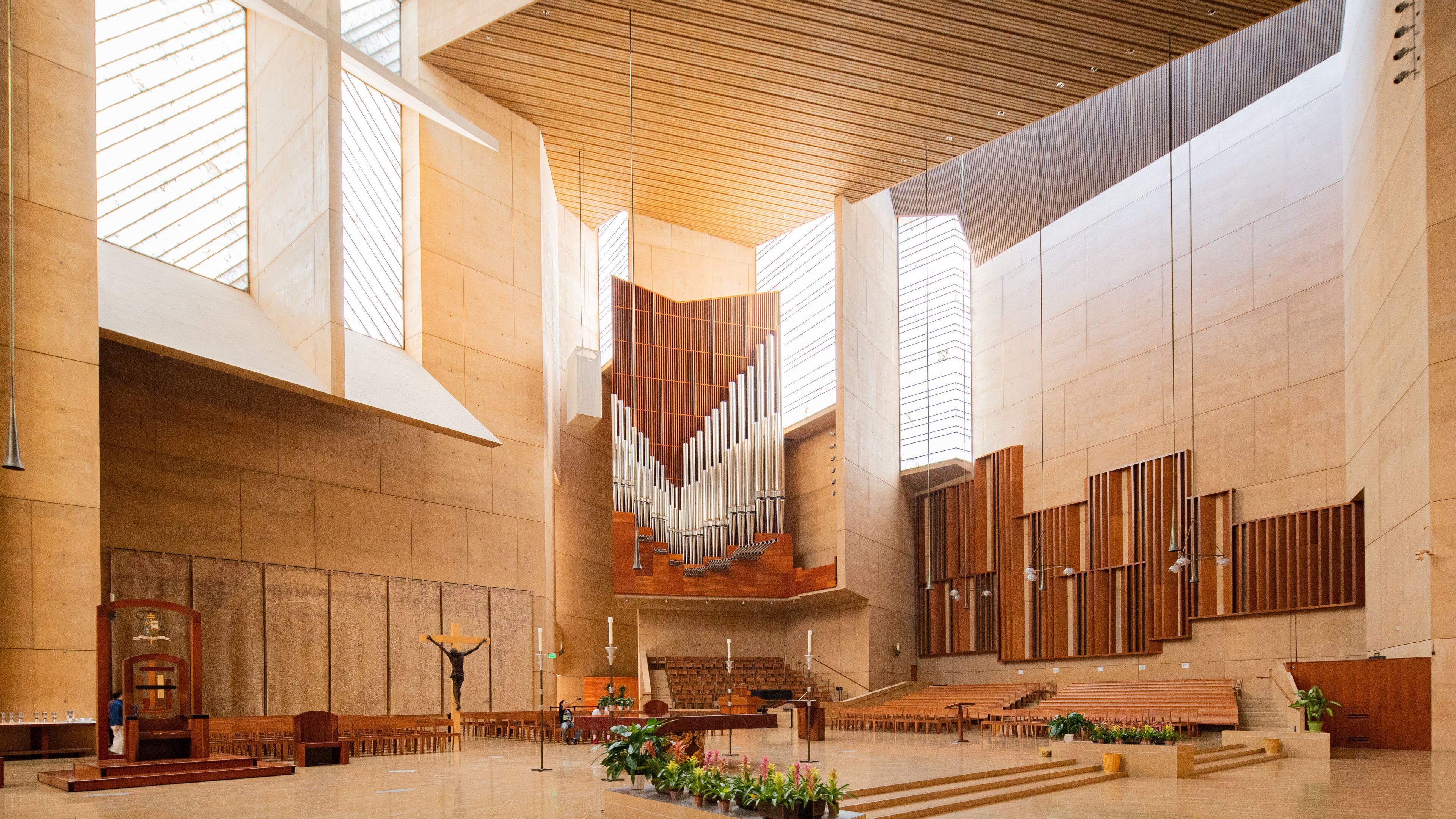 A spacious church interior with a wooden organ, pews, and a crucifix.