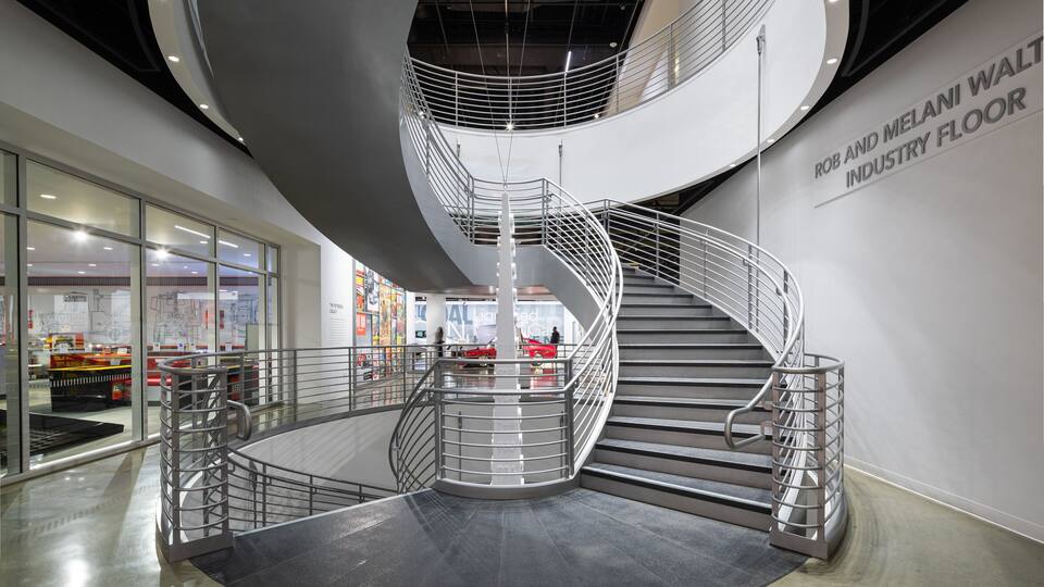Ein modernes Interieur mit einer Wendeltreppe, Glaswänden und einem Schild mit der Aufschrift 'ROB AND MELANI WALT INDUSTRY FLOOR'.
