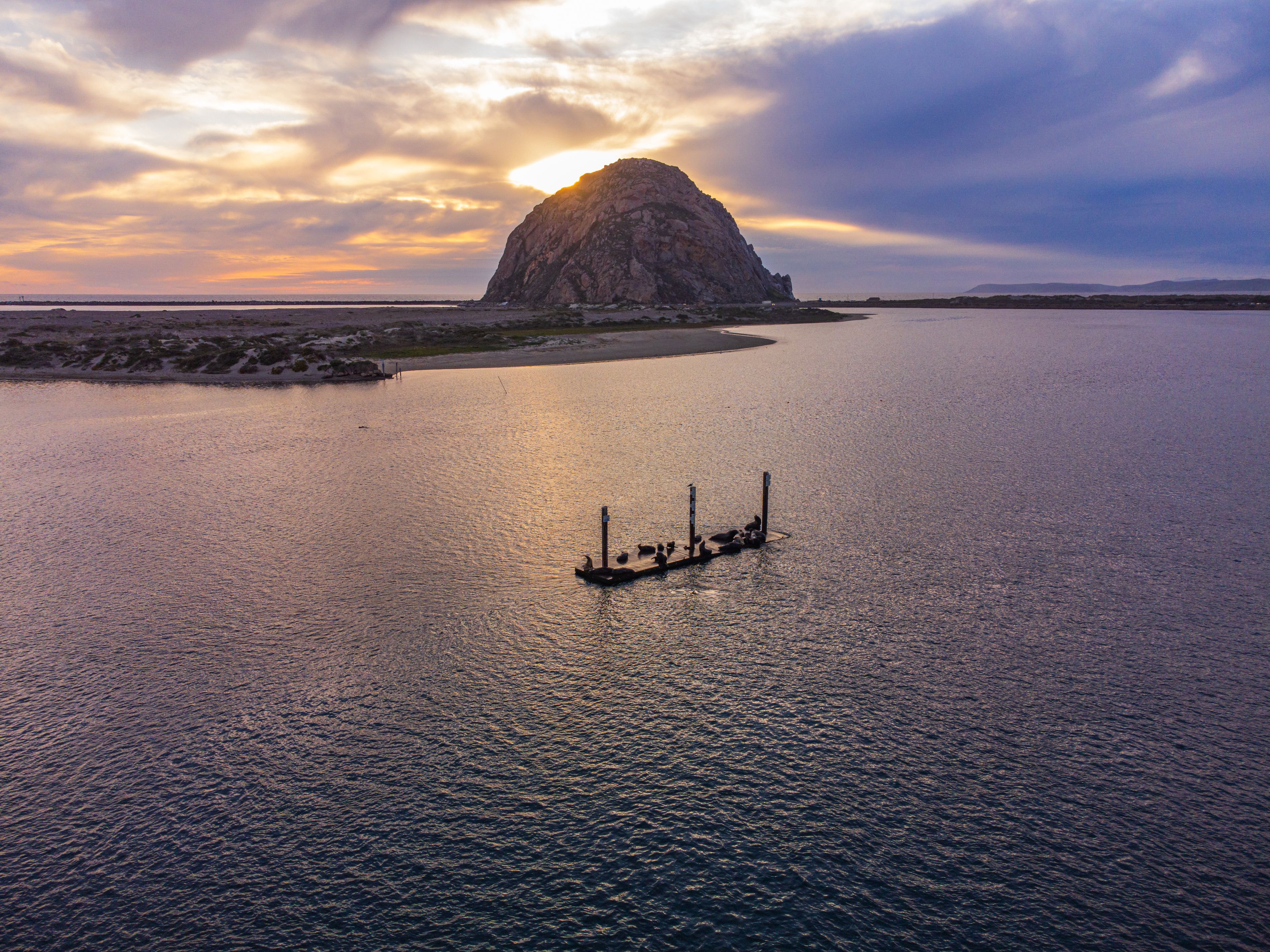 Morro bay, California, aerial view of the Morro Bay rock and of sea lions lying on a wooden dock in the middle of the bay. Sunset, cloudy sky, colorfu