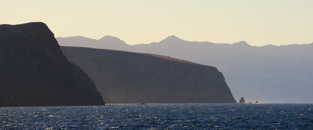 A coastal landscape with a prominent cliff and distant mountains.