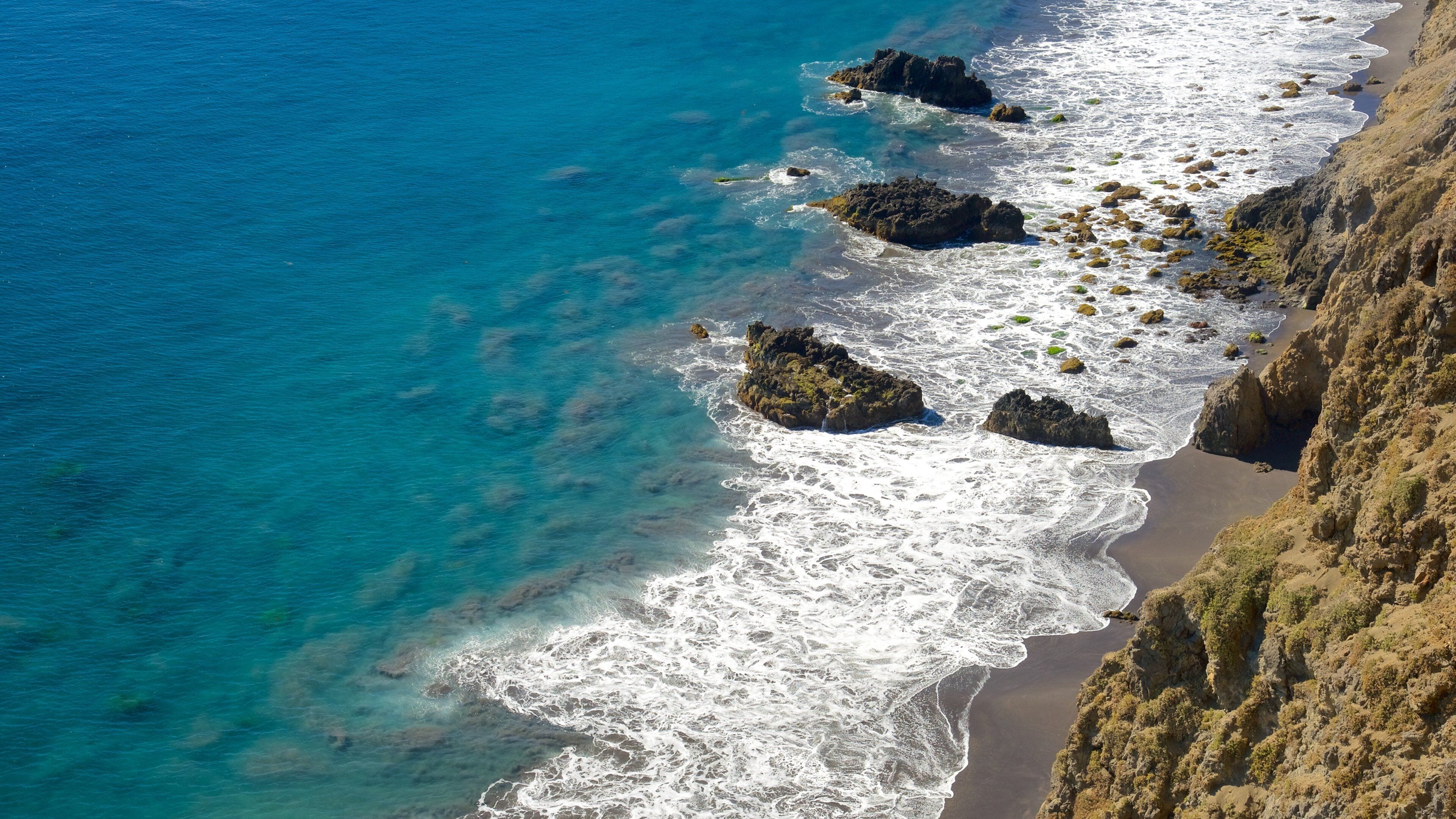 Un paisaje costero con aguas azul cristalino, afloramientos rocosos y una playa arenosa.