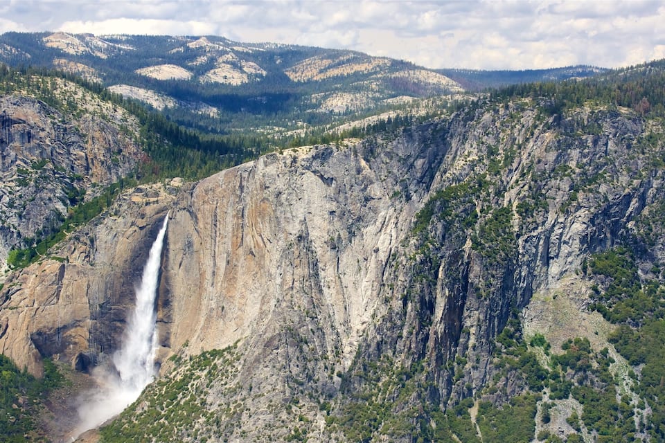 A waterfall cascading down a steep cliff surrounded by forested mountains.