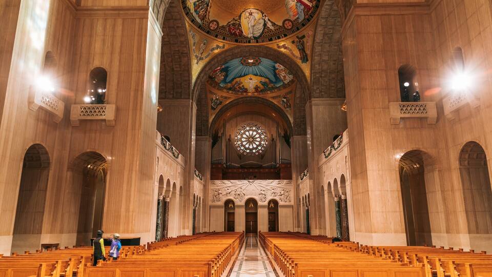A grand cathedral interior with high vaulted ceilings, ornate stained glass windows, and rows of wooden pews.