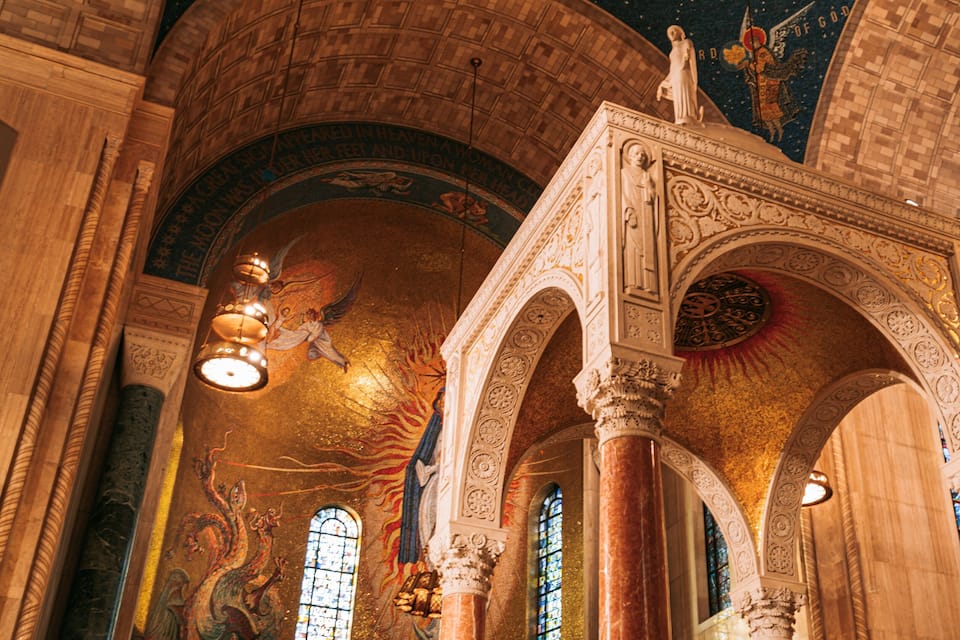 An ornate interior with high vaulted ceilings, detailed frescoes, and stained glass windows.