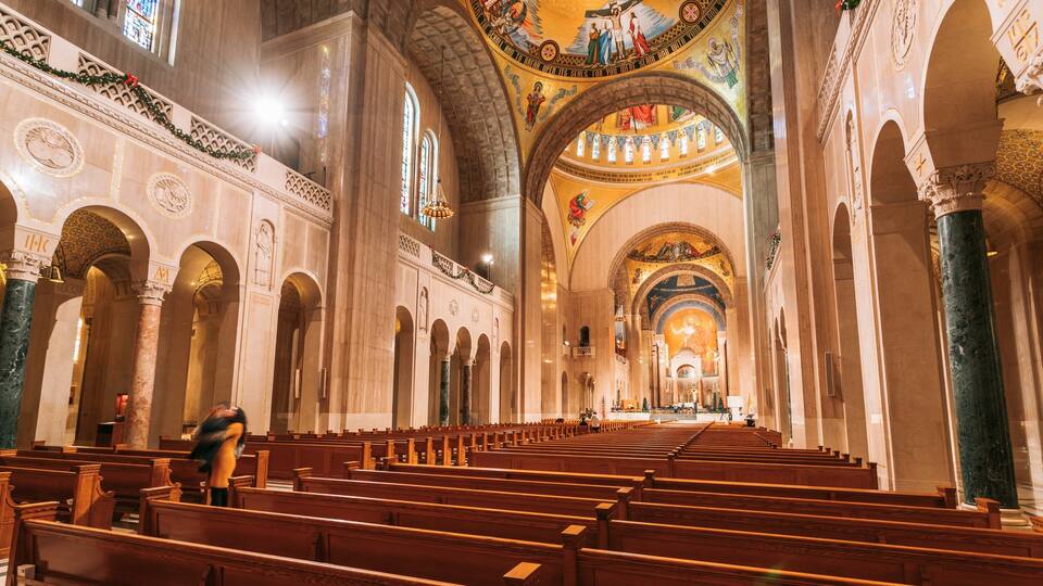 An interior of a church with high arched ceilings, wooden pews, and detailed wall decorations.