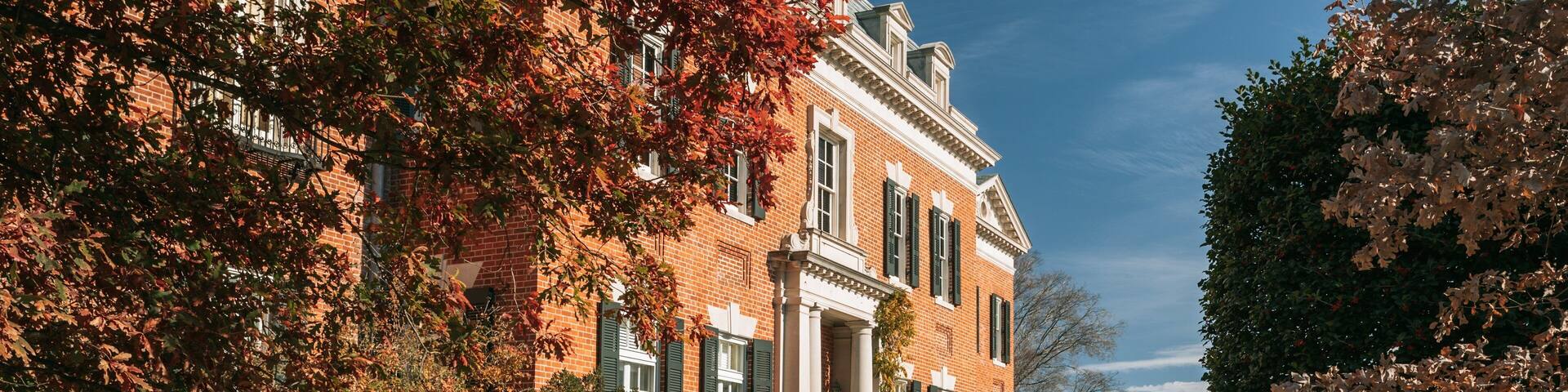A brick building with green shutters, surrounded by trees with autumn leaves.