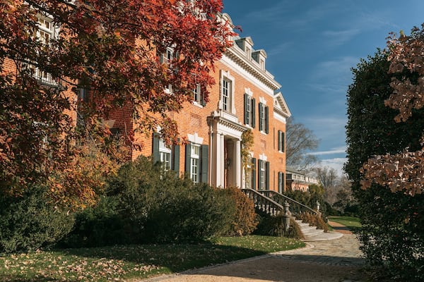 Un bâtiment en briques avec des volets verts, entouré d’arbres aux feuilles d’automne.