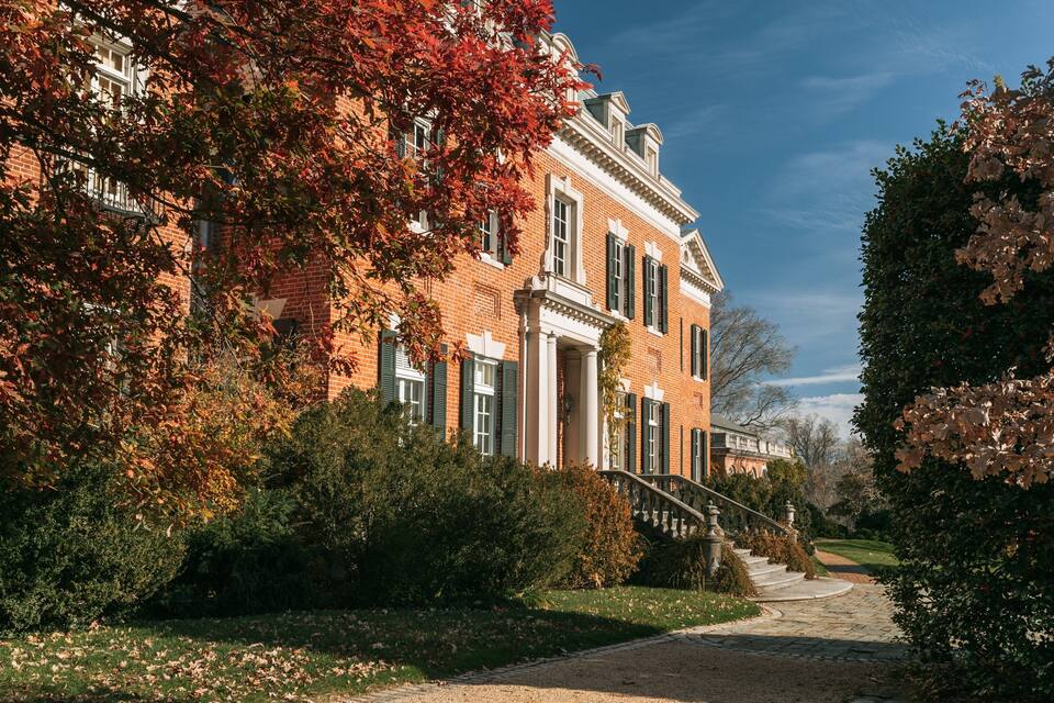 Ein Backsteinhaus mit grünen Fensterläden, umgeben von Bäumen mit Herbstlaub.