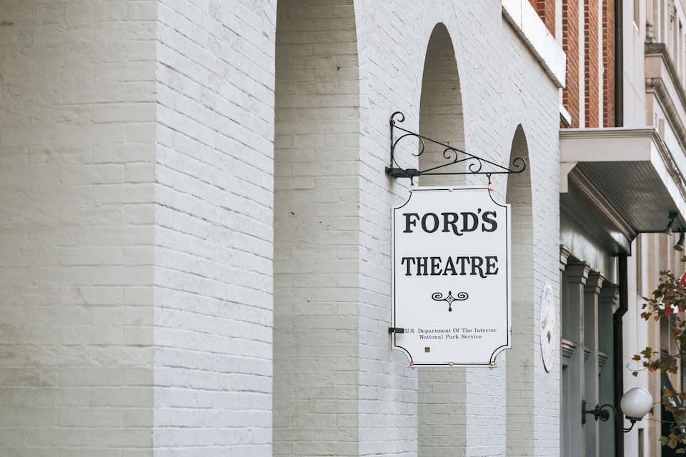 Een wit bakstenen gebouw met een bord waarop staat 'FORD'S THEATRE' en een bord van het U.S. Department of the Interior National Park Service.