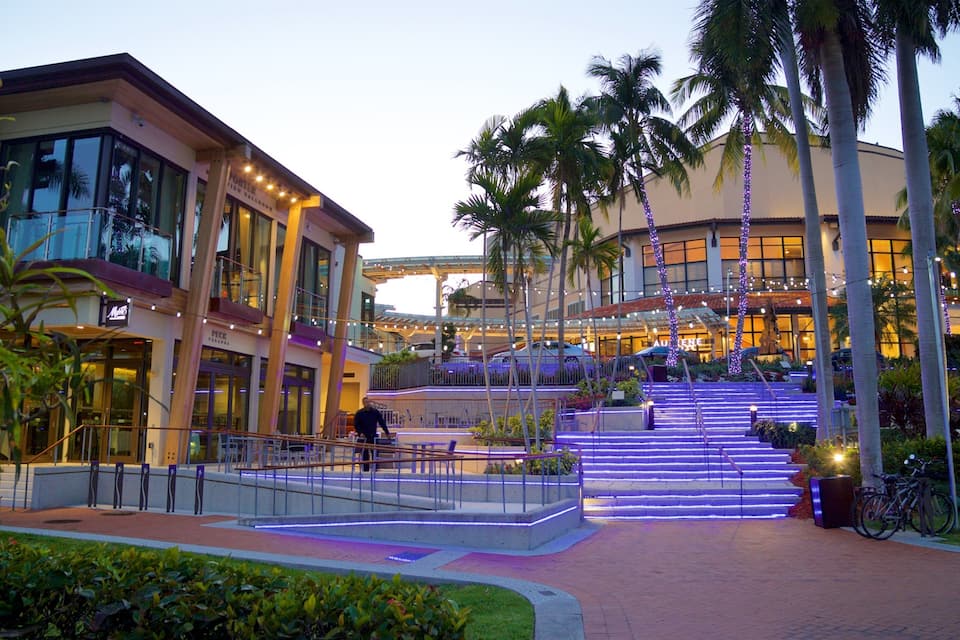 A modern building with glass windows, palm trees, and a staircase with blue lights.