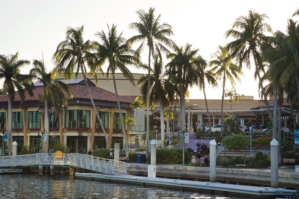 A waterfront with a bridge, palm trees, and a building with a red roof.
