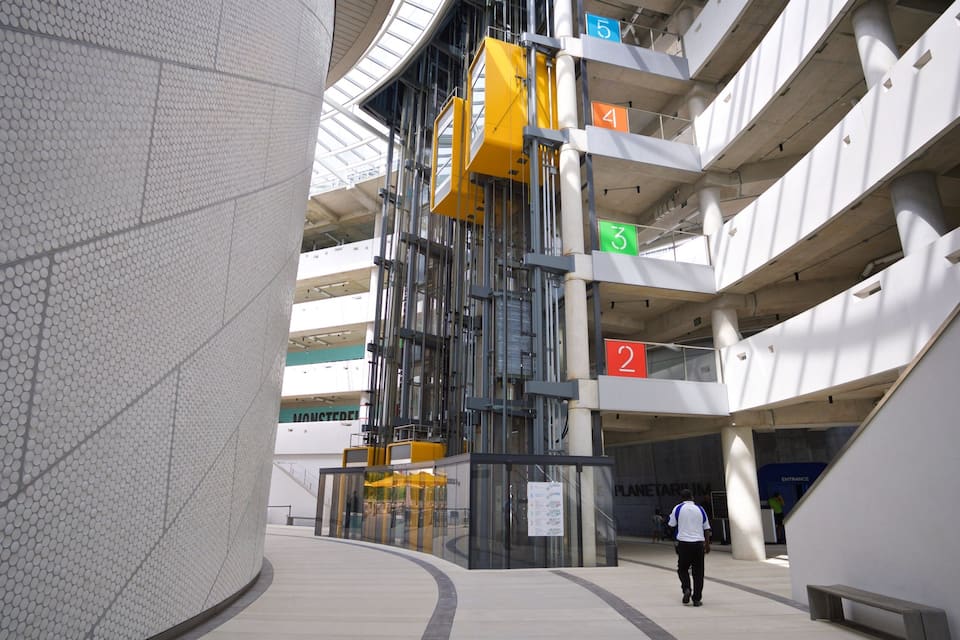 Una estructura arquitectónica moderna con varios niveles, barandillas de vidrio y un patrón geométrico distintivo en un lateral.