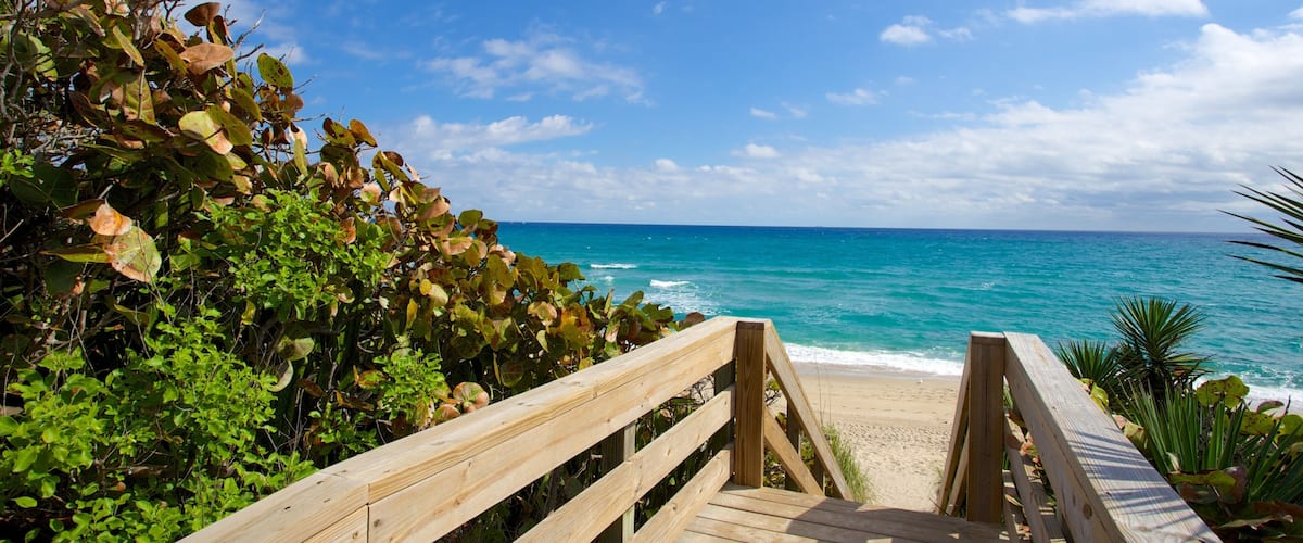 A wooden boardwalk leading to a beach with turquoise water and a clear sky.