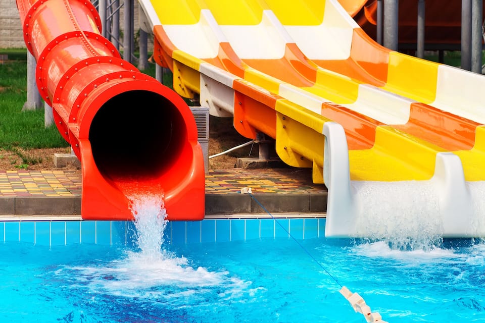 A water slide with a red and yellow design, leading into a pool.
