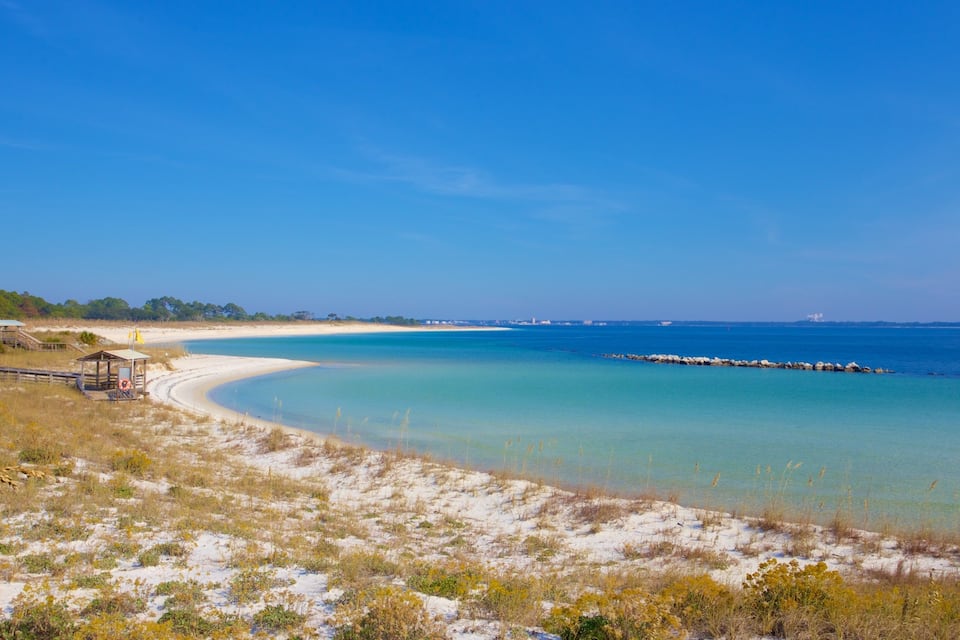 A beach with clear turquoise water, a sandy shoreline, and a wooden pier.