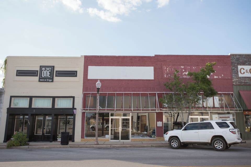 A street with a white SUV parked in front of a building with a sign that reads "ONE THIRTY ONE EVENTS BY TRIGO".