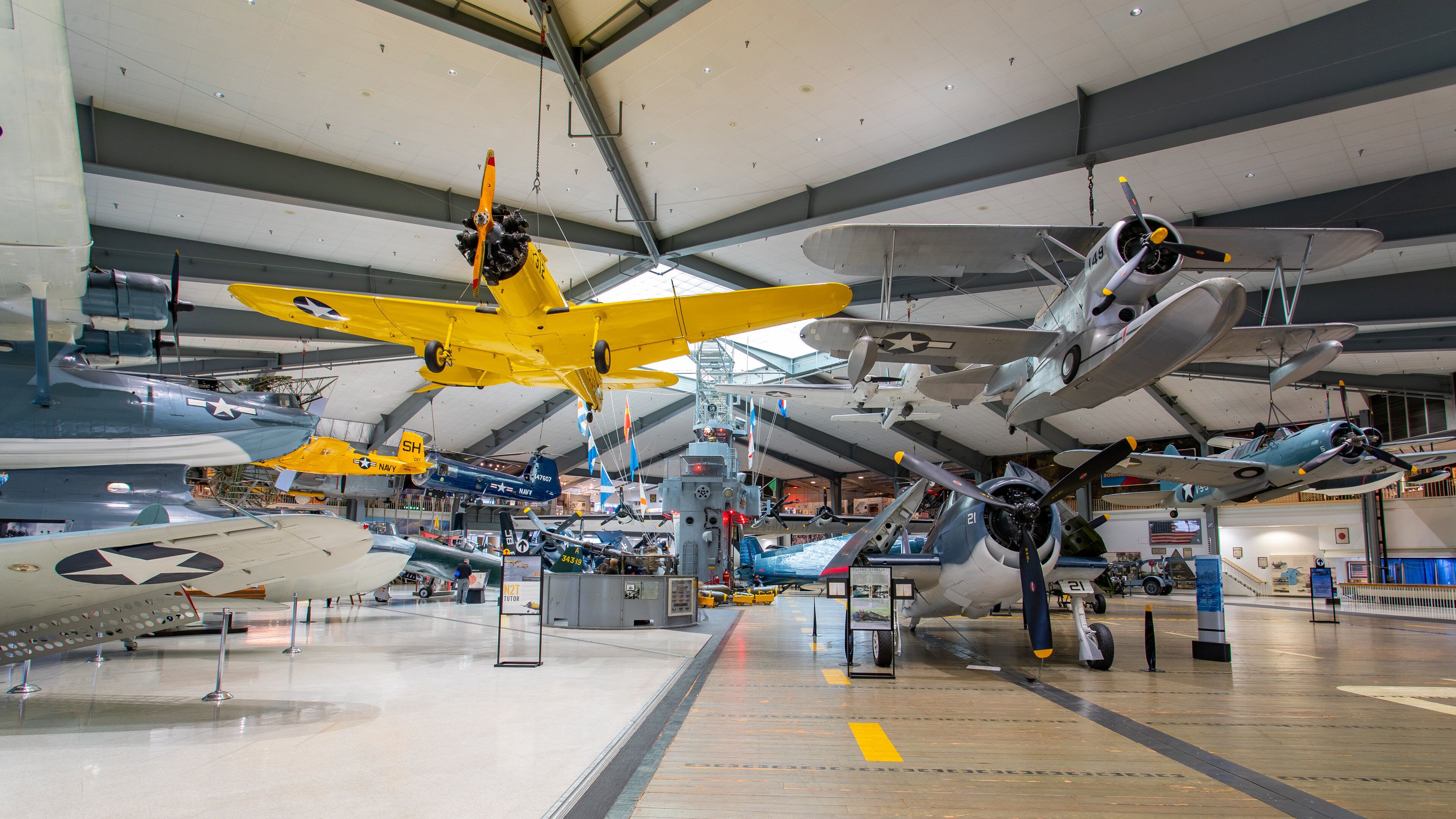 A museum with various aircraft on display, including a yellow plane and a silver plane with a star emblem.