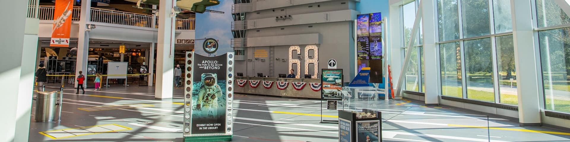 A museum with a large aircraft suspended from the ceiling, a '68' sign, and exhibits related to space exploration.