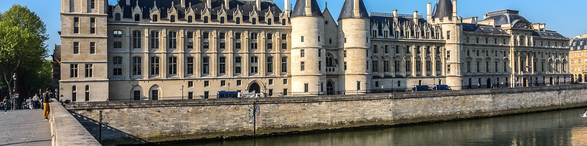 Um edifício histórico com várias torres e um rio ao primeiro plano.