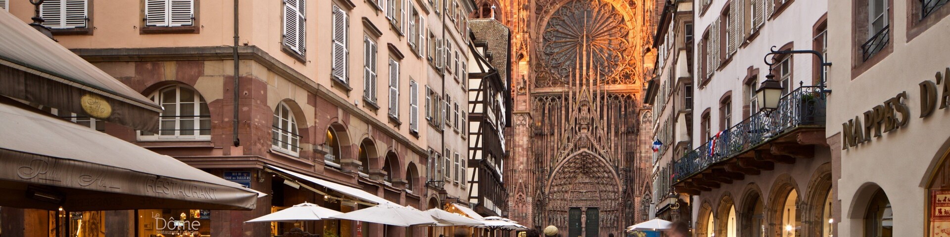 Una calle empedrada con edificios históricos, cafés al aire libre y una catedral al fondo.