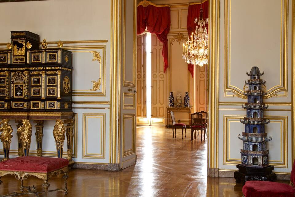 Una habitación opulenta con muebles ornamentados, una lámpara de araña imponente y un detallado aparador de madera.
