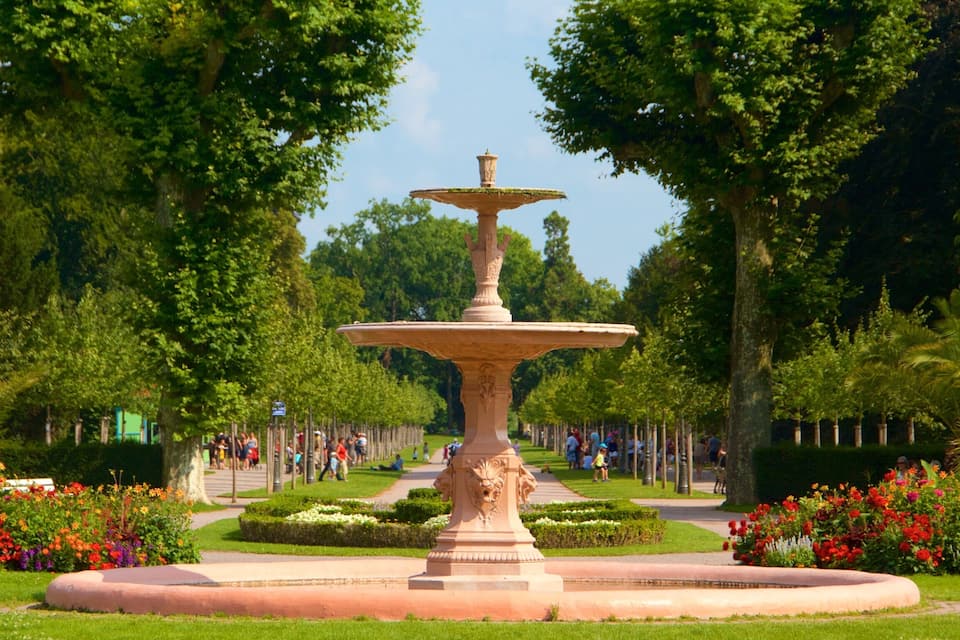 A tiered fountain with a lion base, surrounded by lush greenery and flowering plants.