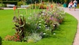 A well-maintained garden with a variety of colorful flowers and plants, a grassy path, and a bench in the background.