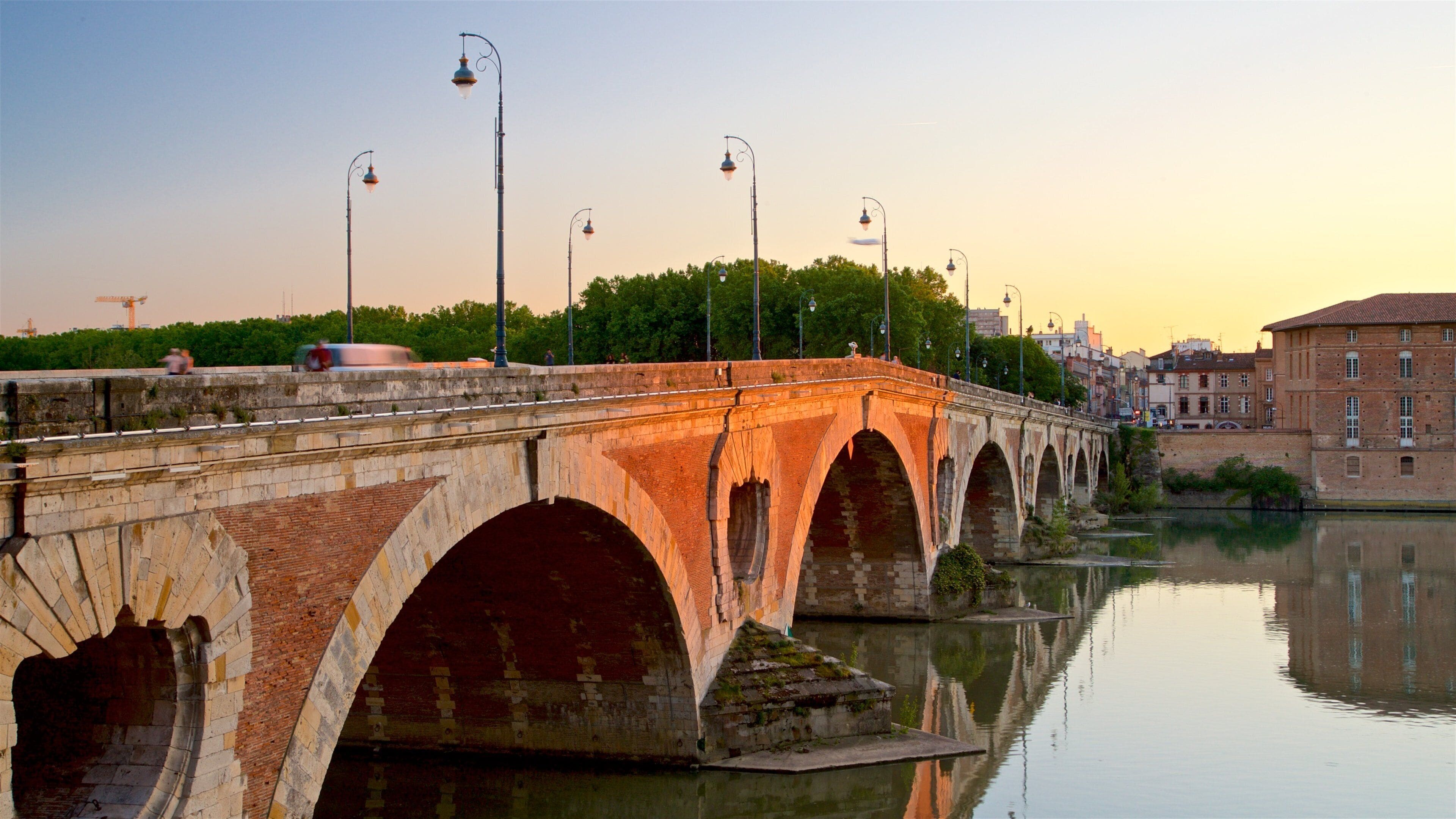 Un puente de piedra sobre un río tranquilo, con un atardecer de fondo.