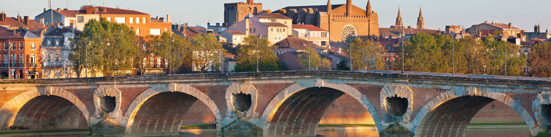 Un puente de piedra con varios arcos sobre un río, con edificios y una iglesia al fondo.