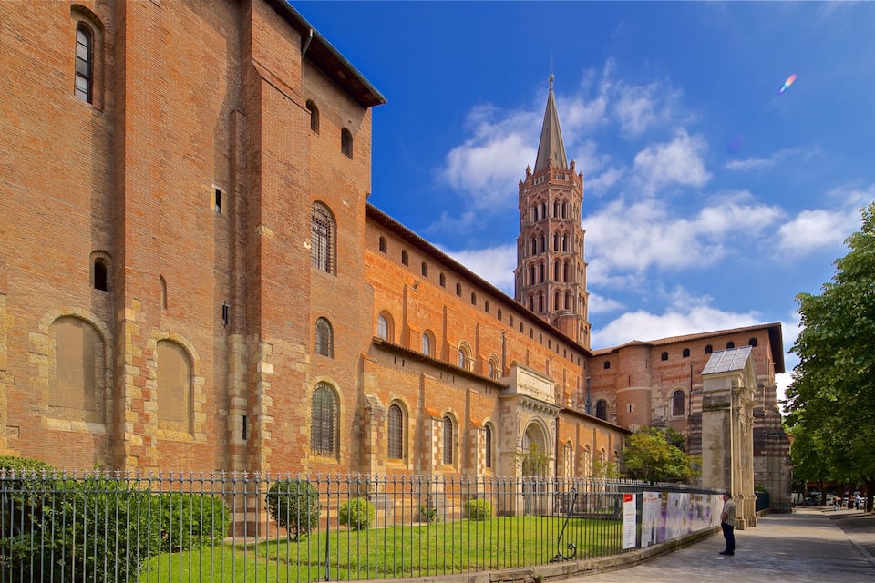 A historic brick building with arched windows and a tall tower in the background.
