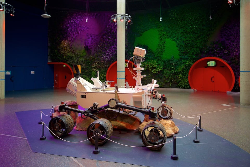 A Mars rover model displayed in an indoor exhibit with a green and purple wall background.