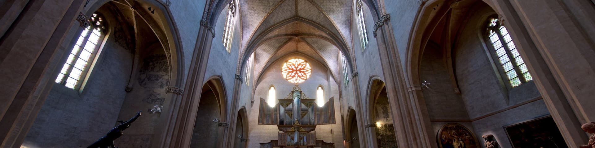 A cathedral interior with high vaulted ceilings, large stained glass windows, and a central altar.