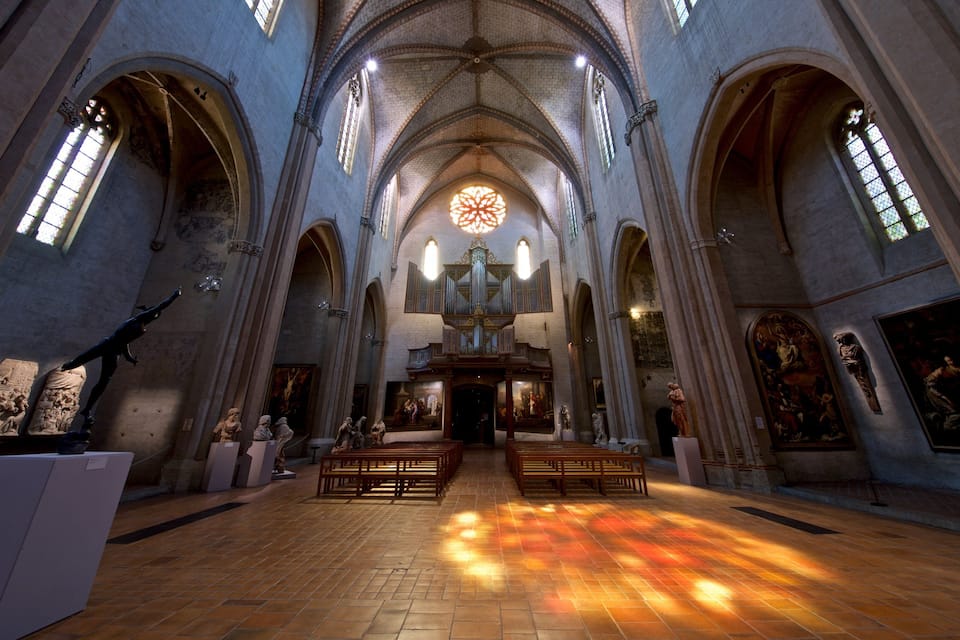 A cathedral interior with high vaulted ceilings, large stained glass windows, and a central altar.