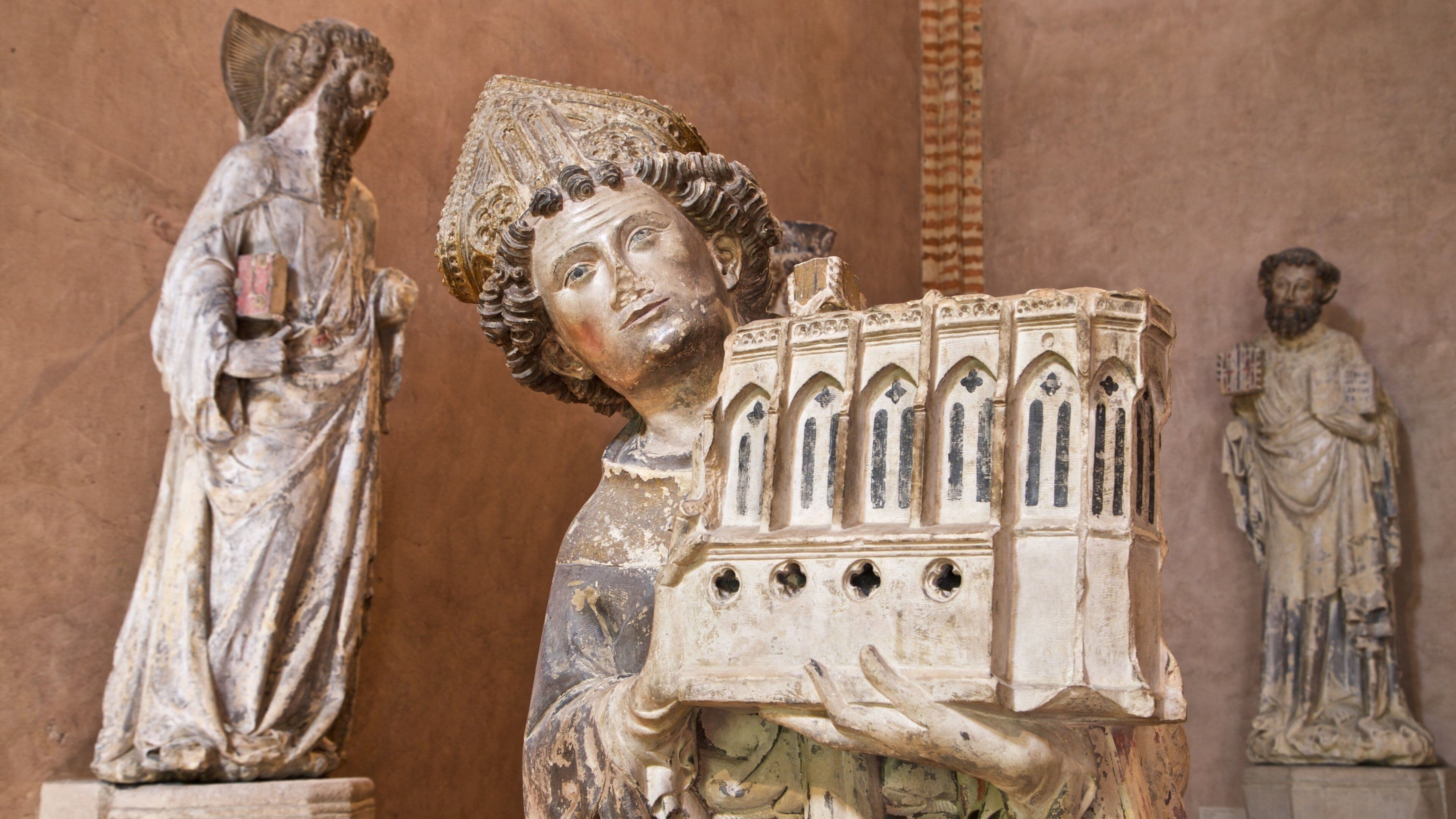 A statue of a robed figure holding a book with Gothic architectural elements.