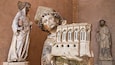 Eine Statue einer in Gewändern gekleideten Figur, die ein Buch hält, mit gotischen architektonischen Details.