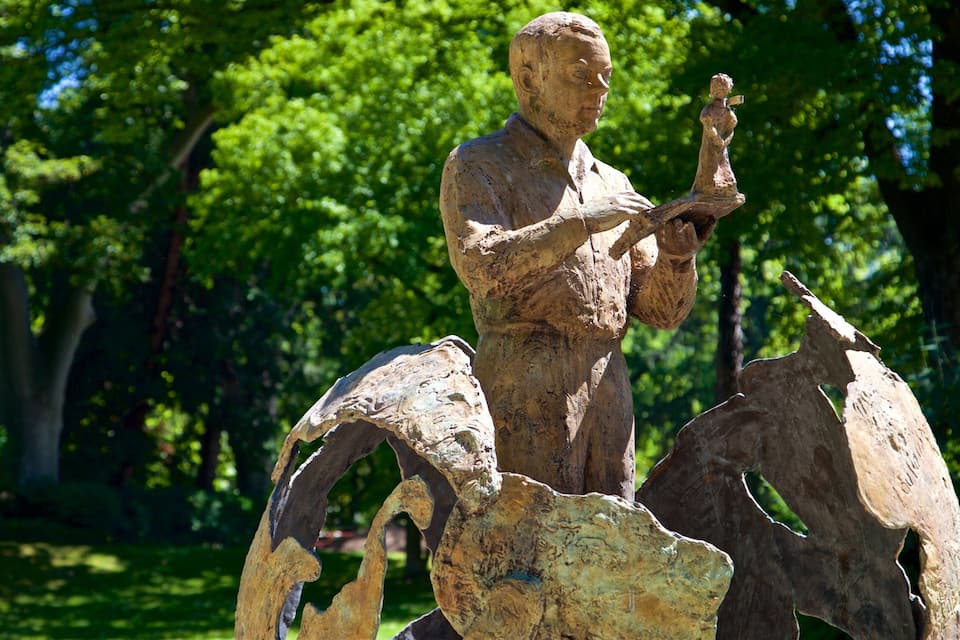A bronze statue of a man holding a book in a park with trees in the background.