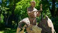 A bronze statue of a man holding a book in a park with trees in the background.