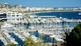 Un puerto deportivo lleno de numerosos barcos, con un paisaje urbano al fondo y un cielo azul despejado.