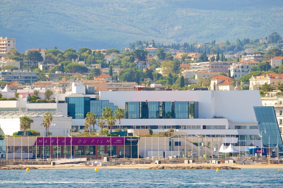 A coastal cityscape with modern architecture, including a distinctive building with a sloped roof and reflective glass windows.