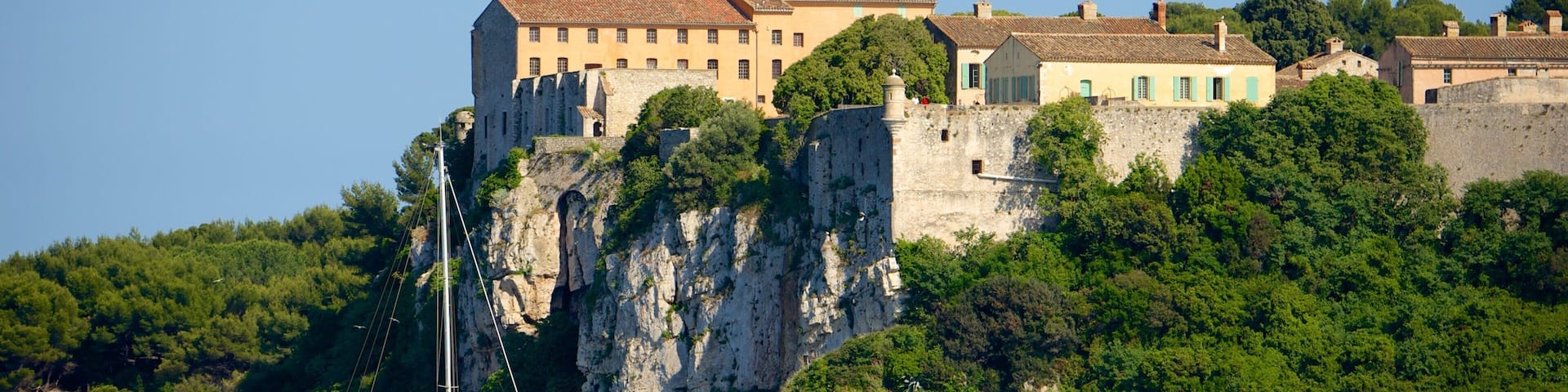 A coastal town with a prominent castle atop a cliff, surrounded by lush greenery and a clear blue sea.